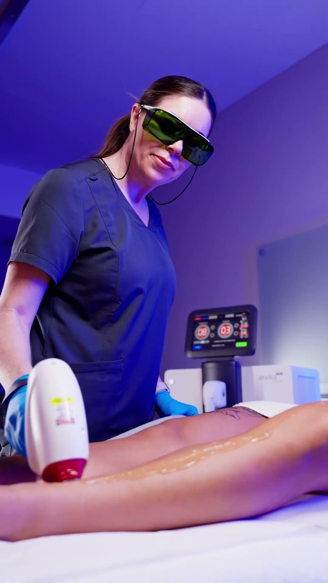 Practitioner in goggles performing laser hair removal on a client’s leg